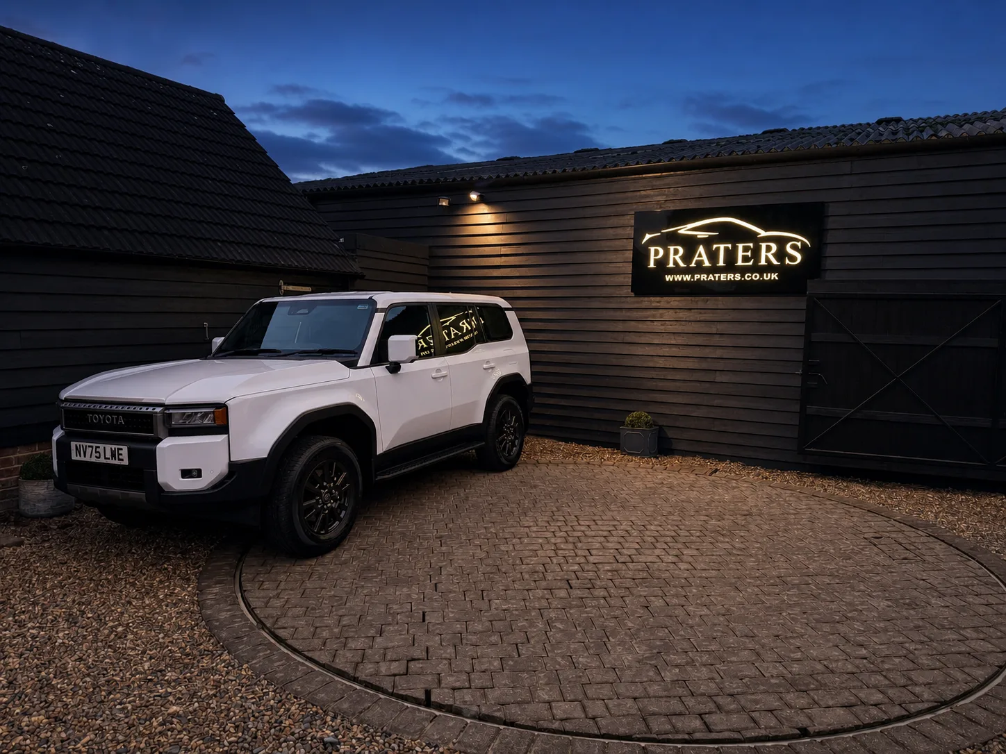 Illuminated Praters exterior sign on a black-clad automotive premises