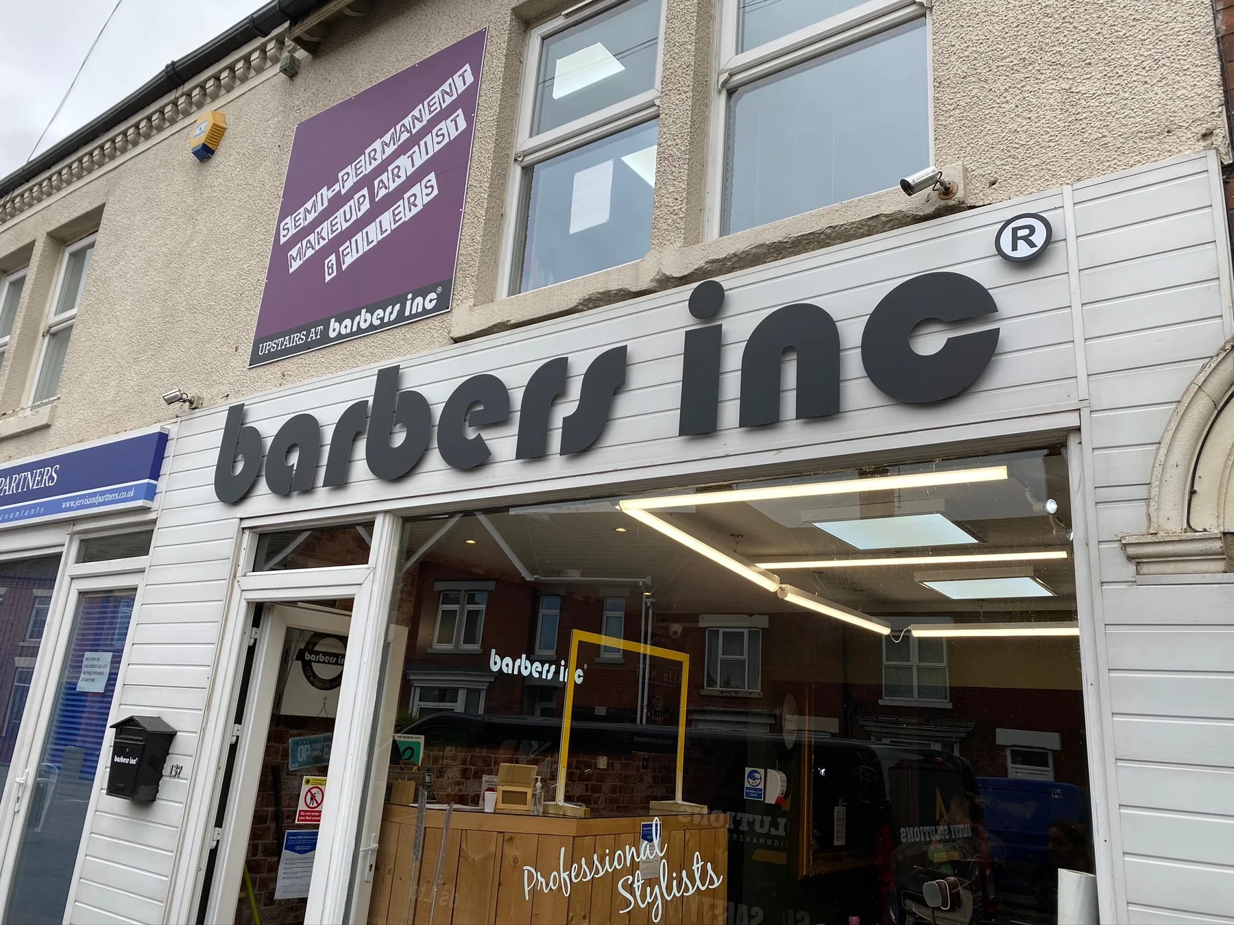 Raised black Barbers Inc lettering fitted across a white shopfront fascia