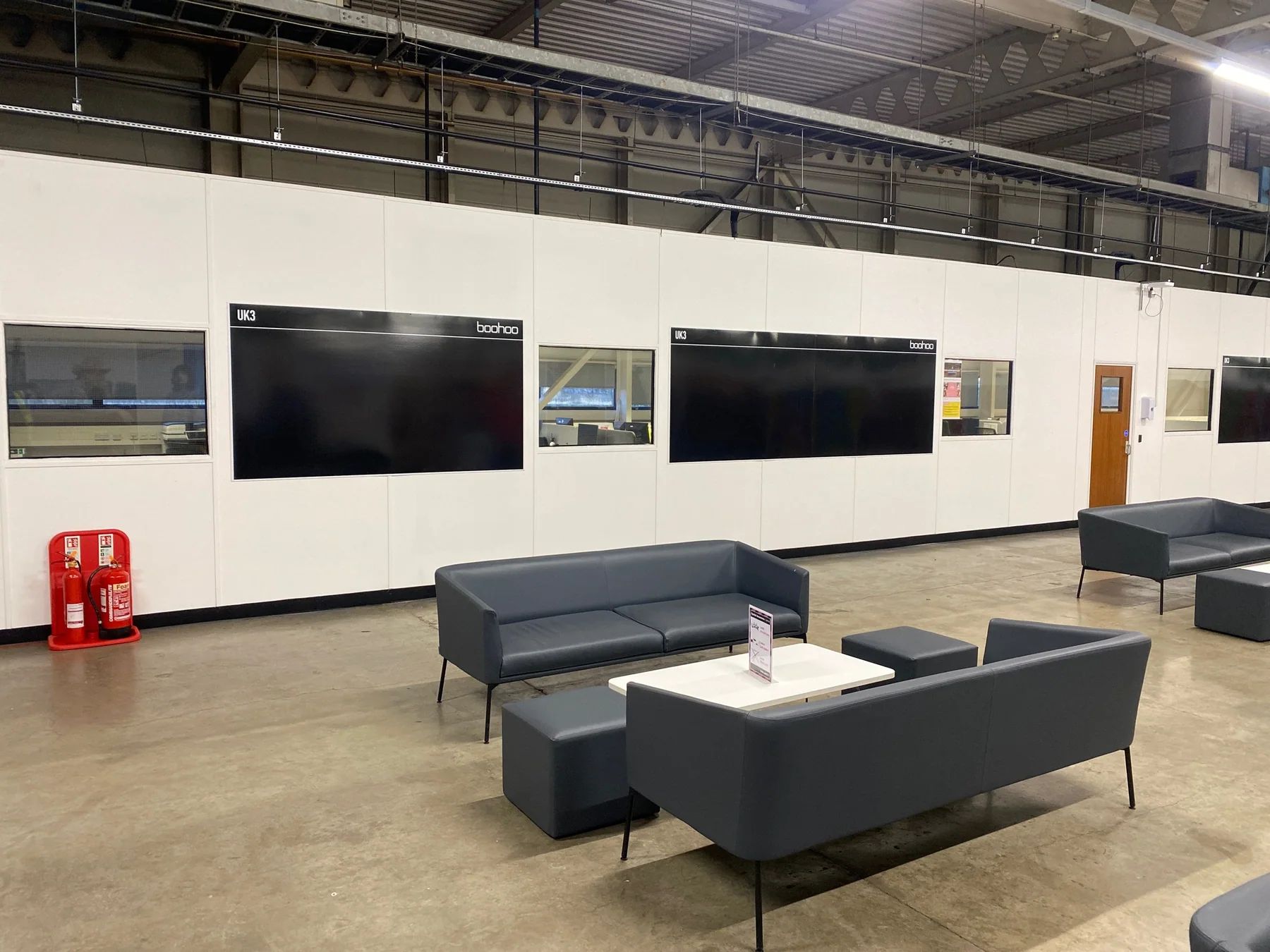 Black Boohoo operational display boards fitted across a white warehouse office wall