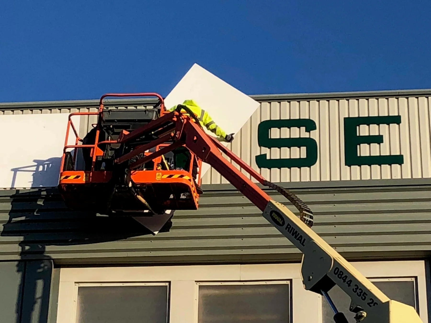Sign installer in an access platform positioning a large letter on an industrial building