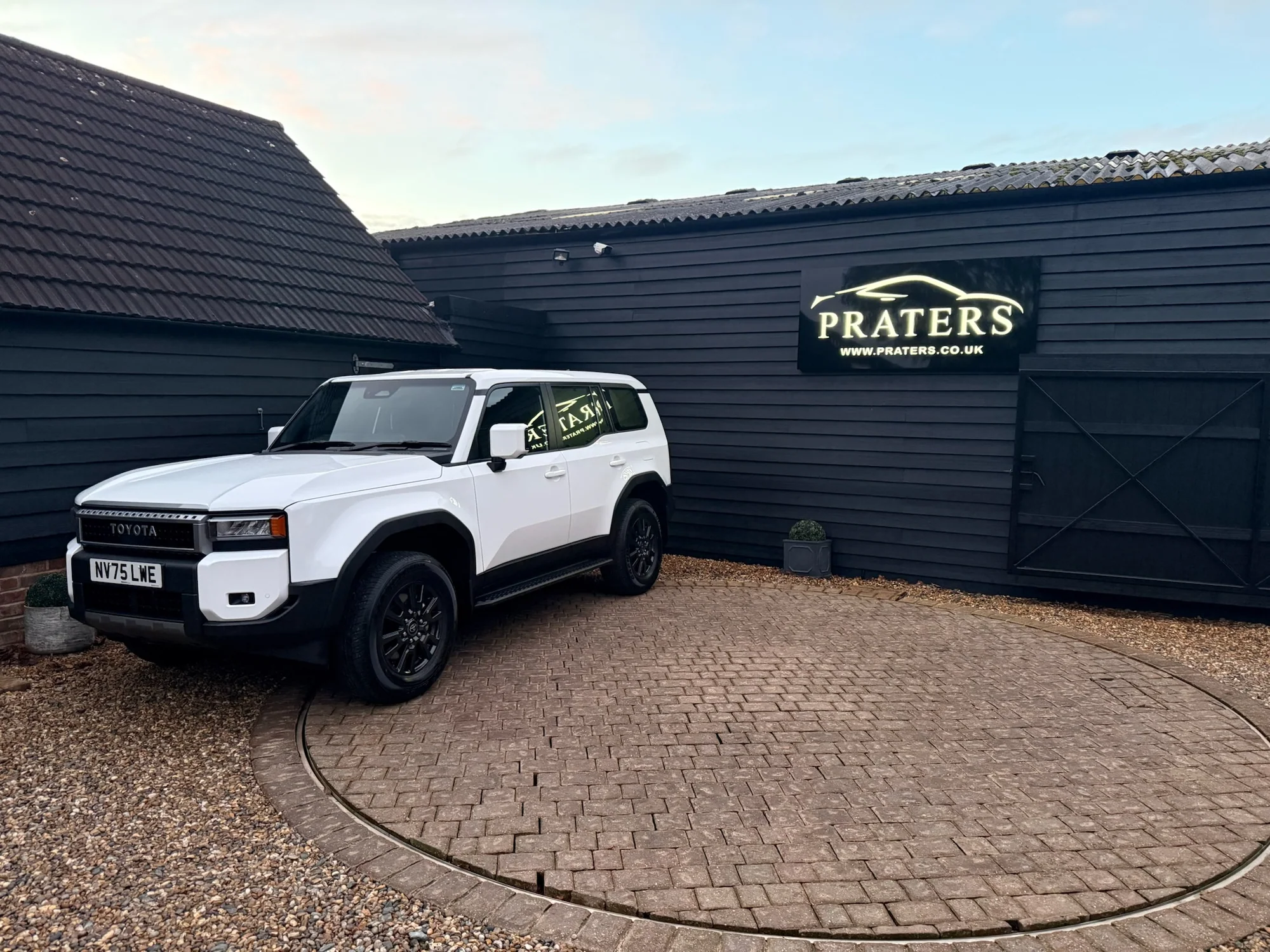 Installed illuminated Praters sign above a white vehicle outside black-clad premises
