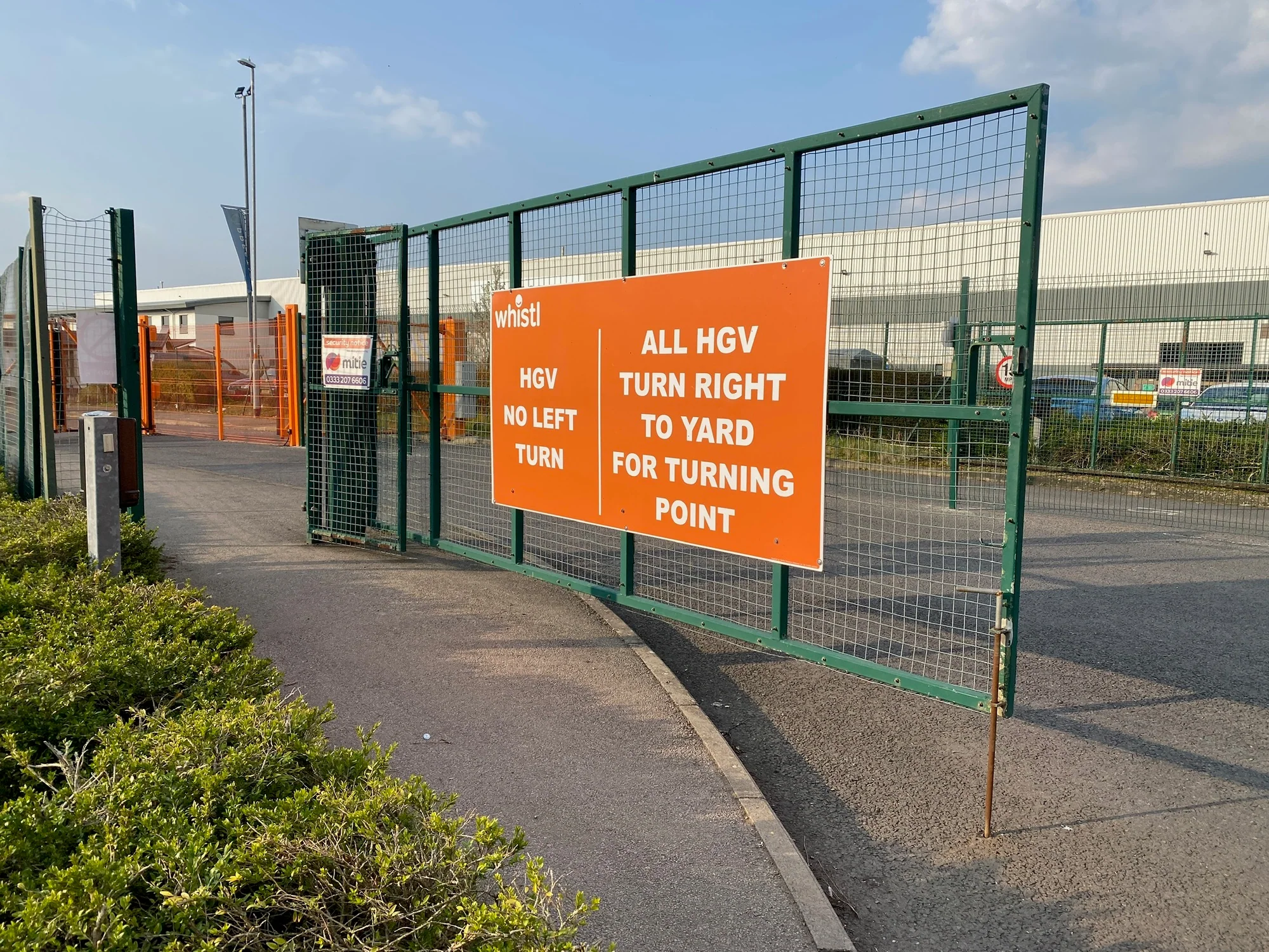 Orange Whistl HGV routing signs across green site gates