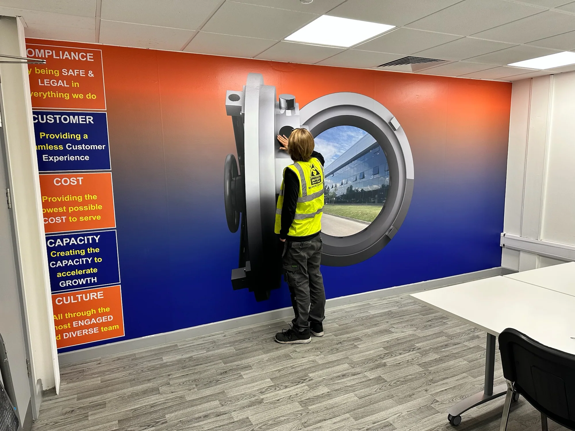 Installer applying an orange and blue B and M workplace graphic around a vault image